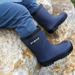 A boy in Rain boot navy sitting down 