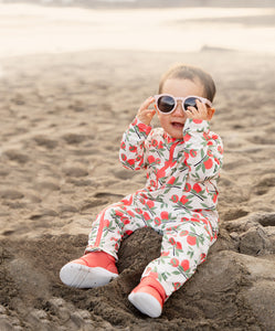 Cute kid wearing stonz sunsuit, cruiser baby shoe and eco sunnies in citrus color sitting at the beach.