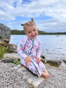 cute kid wearing stonz sunsuit in meadow color sitting on a rock at the beach.