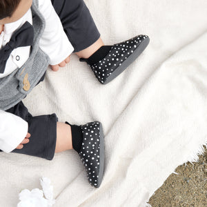 Stonz Yale baby shoe in Black - Polka Dot, shown on an infant sitting on a white blanket.