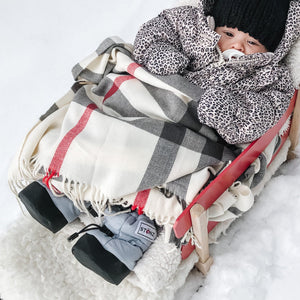 Stonz Puffer Baby Winter Booties in Haze Blue, on an infant wrapped in a plaid blanket laying on a sled in snow.