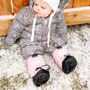 Stonz Puffer Baby Booties in Haze Pink, on an infant sitting outdoors in the winter.