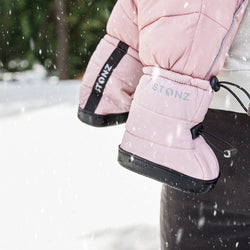 Stonz Puffer Toddler Booties in Haze Pink, worn on an infant held by a caregiver outside in the snow.