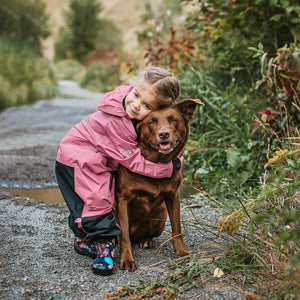 Stonz Rain Suit in Dusty Rose, worn by an infant embracing a dog outside.